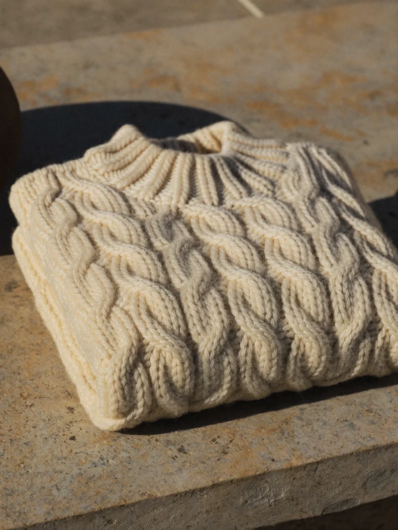Maglione panna a coste grosse piegato su un davanzale in pietra